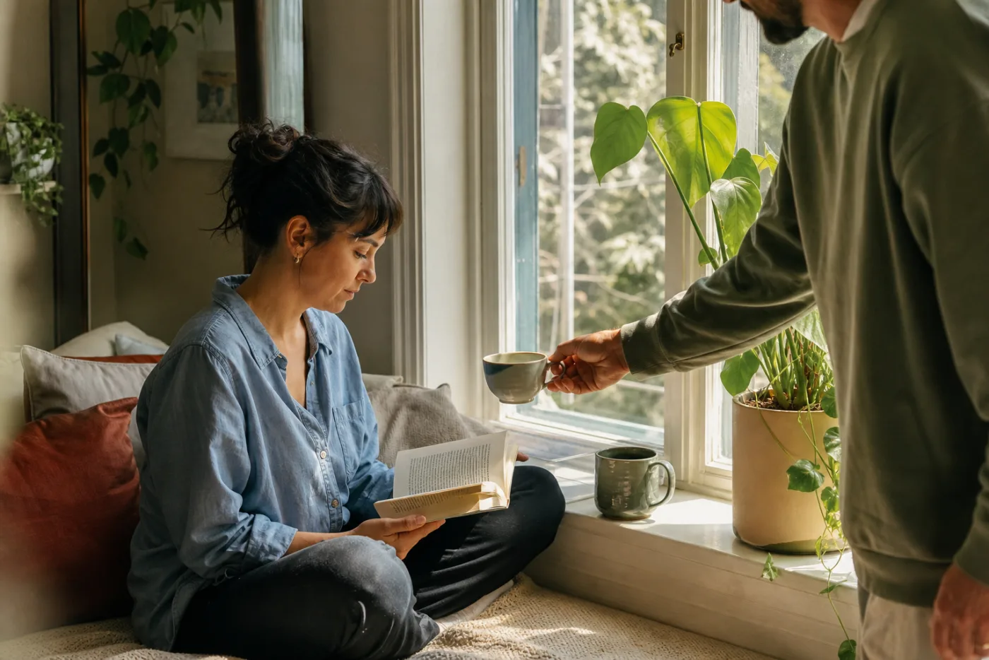 Two neurodivergent adults sharing a quiet room, one offering tea while the other reads by the window.